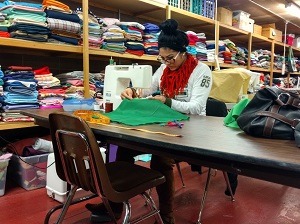 A person sitting at a table sewing on a sewing machine