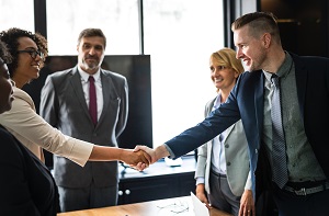 Two people in business attire shaking hands surrounded by a group of people